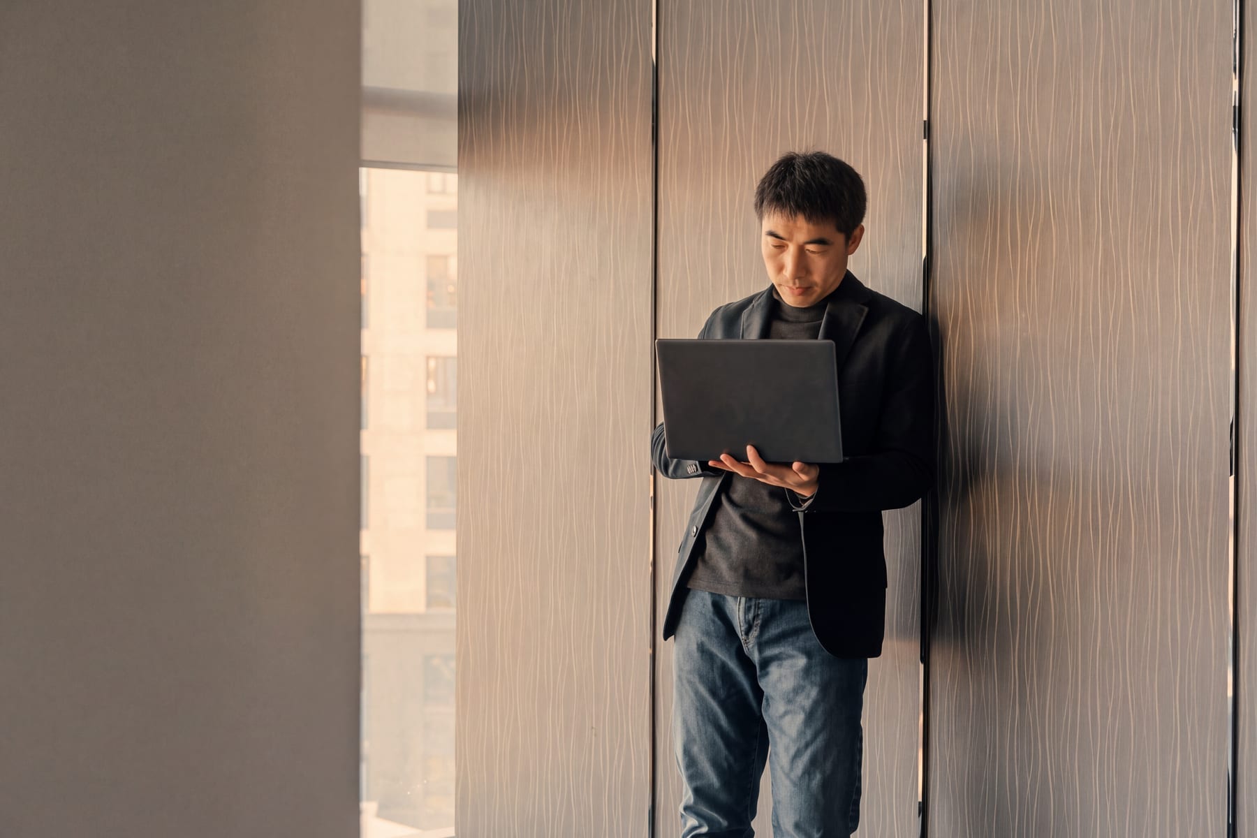 A professional man stands holding an open laptop, reviewing information on the screen with focused attention.